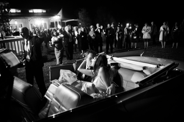 black and white photo of the bride and groom kissing in the backseat of a convertible before they leave the reception - photo by Washington DC based wedding photographers Holland Photo Arts